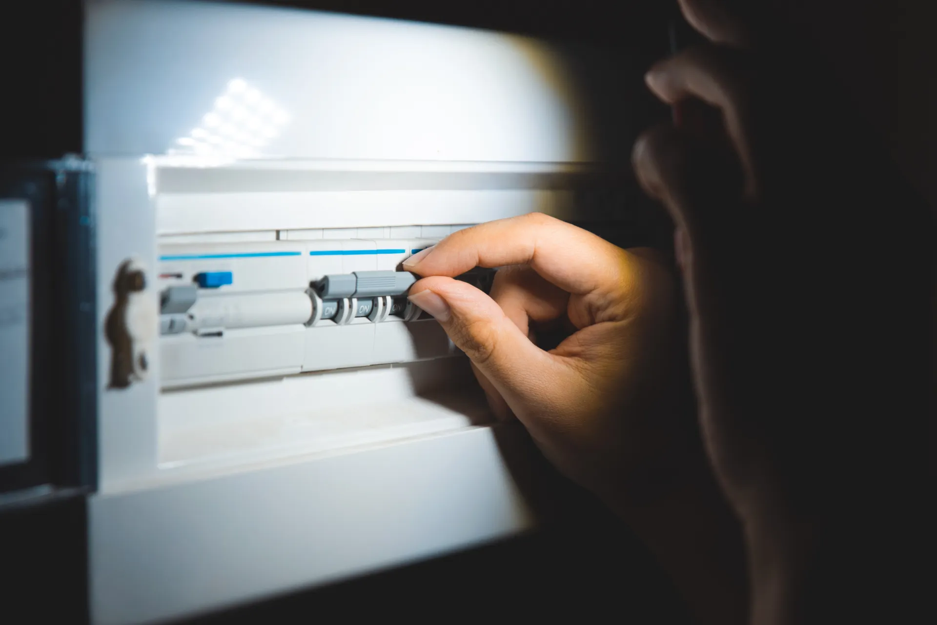 Jemand der an einem Sicherungskasten steht und die Sicherungen versucht einzuschalten, da der Strom ausgefallen ist.