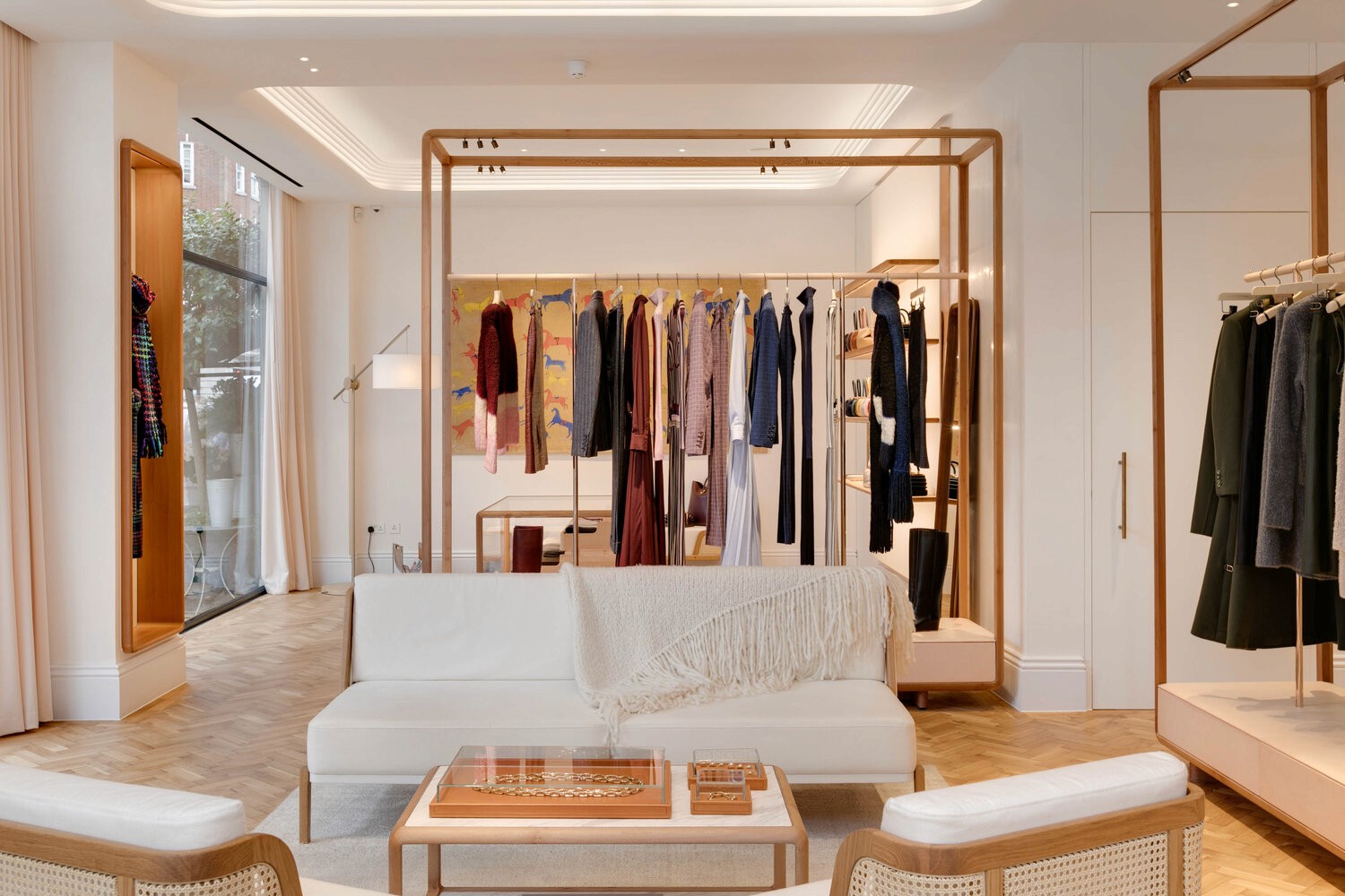 A chic boutique interior with a cozy white sofa, a wicker coffee table, and elegant clothing racks along the walls.