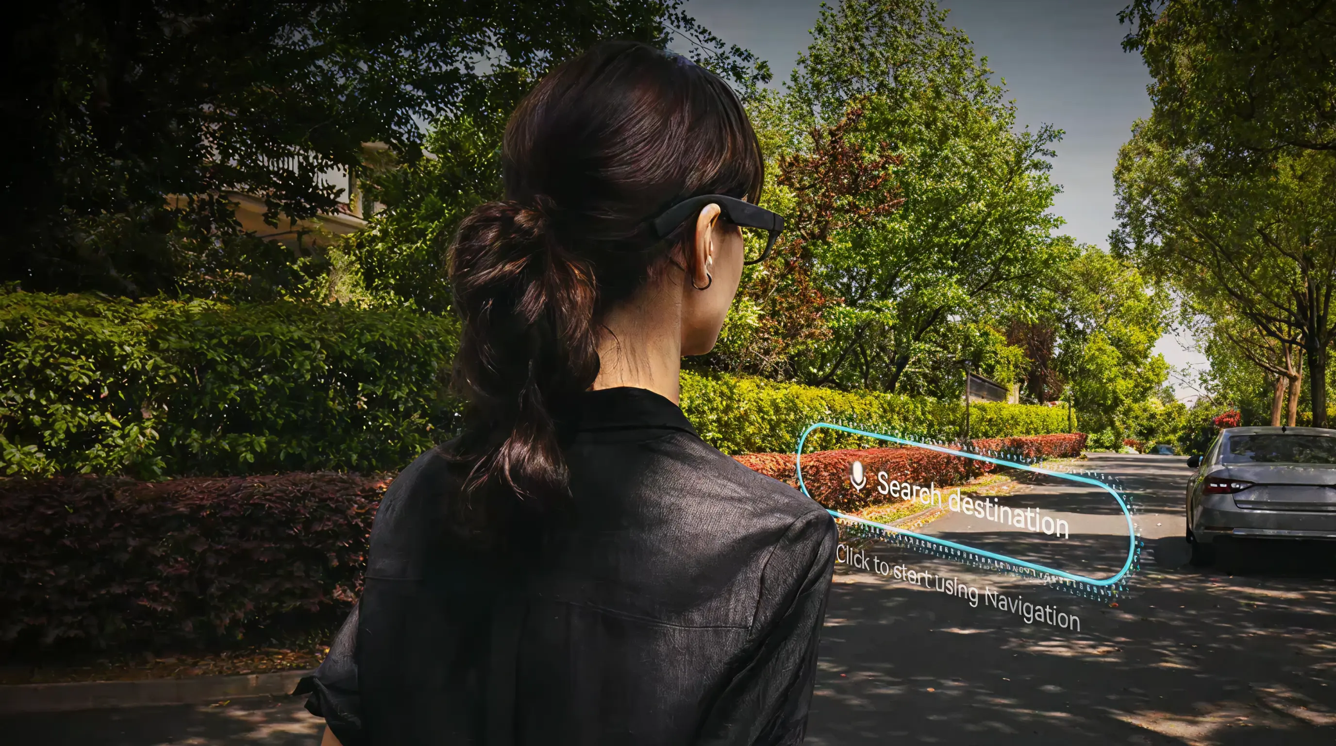 Rear view of a woman wearing slim smart glasses on a tree-lined street. A visual overlay in her field of view shows a "Search destination" prompt and navigation cue, illustrating hands-free turn-by-turn guidance while walking.