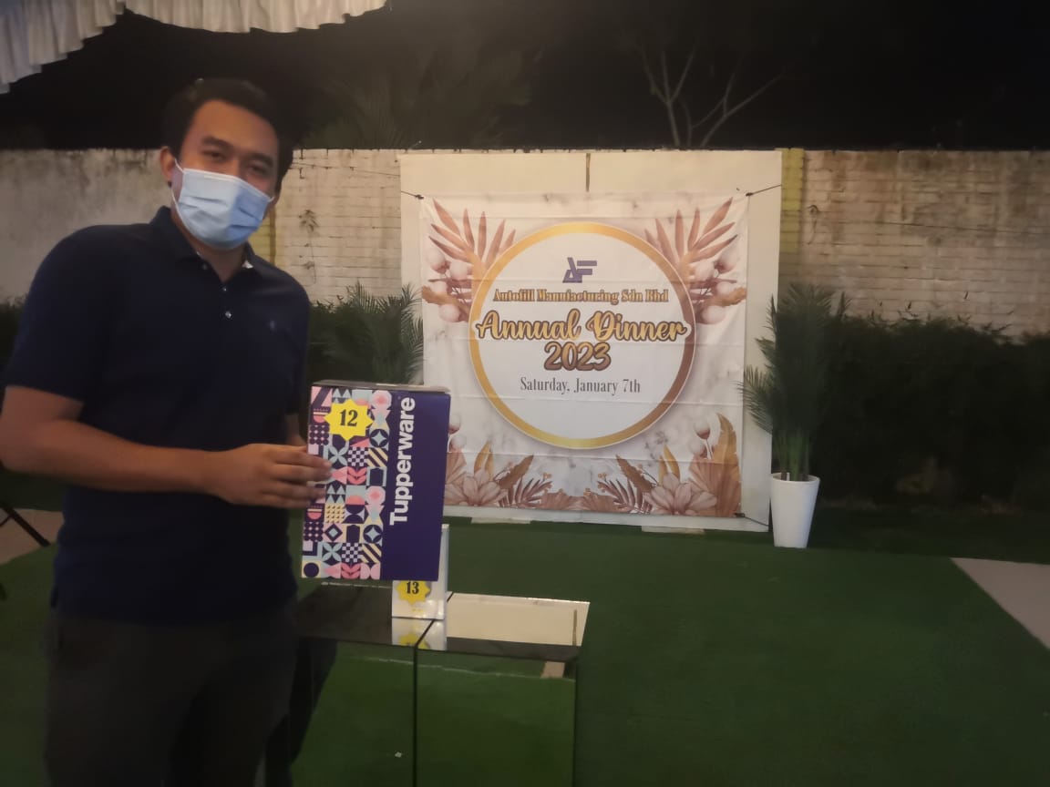 Employee receiving a Tupperware prize at the Annual Dinner 2023, standing in front of the event backdrop.