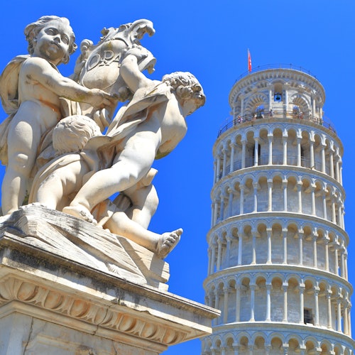 Marble statue of cherubs in foreground with the Leaning Tower of Pisa in the background against a clear blue sky.