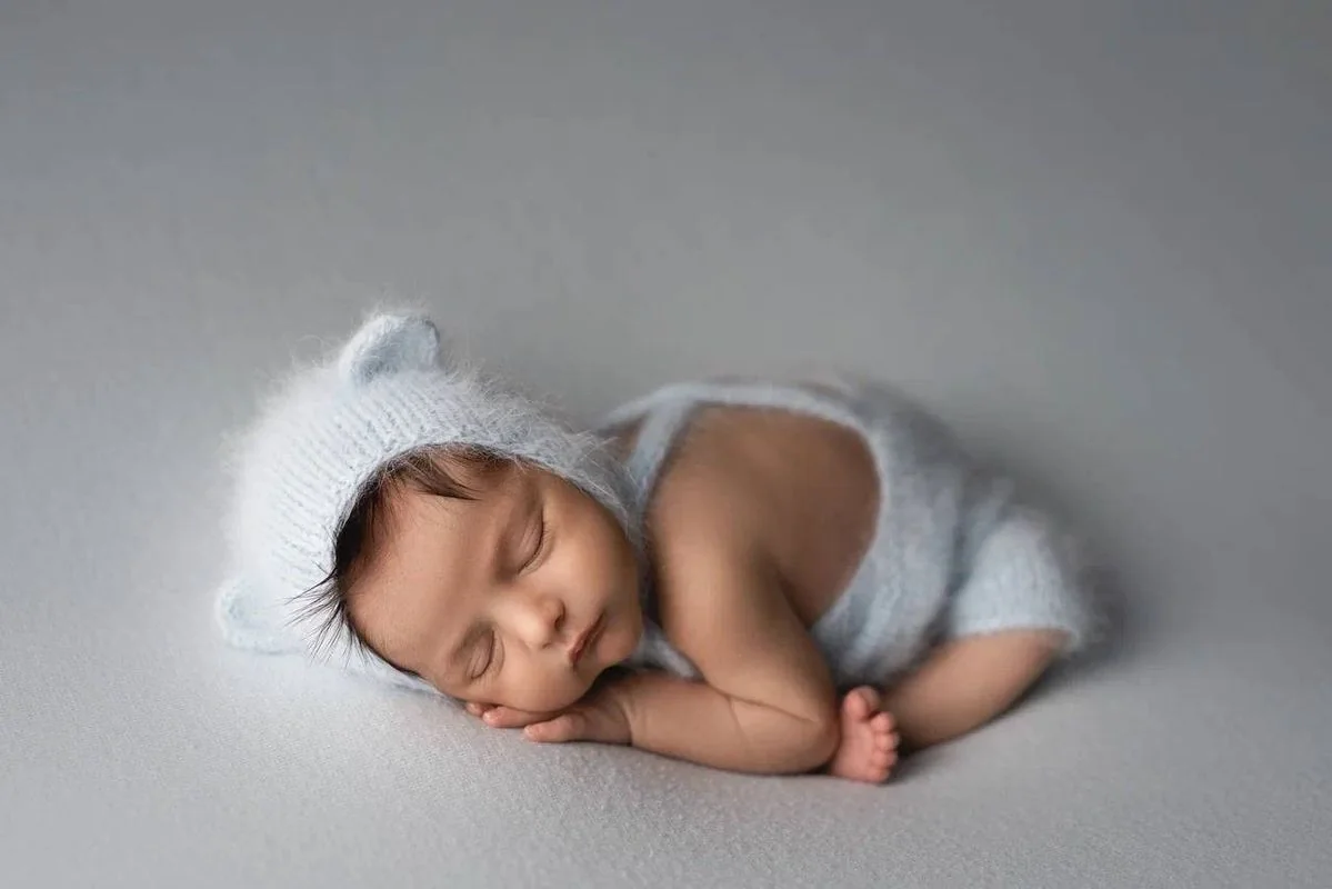 Sleeping baby in a pale blue bear bonnet on grey bedding