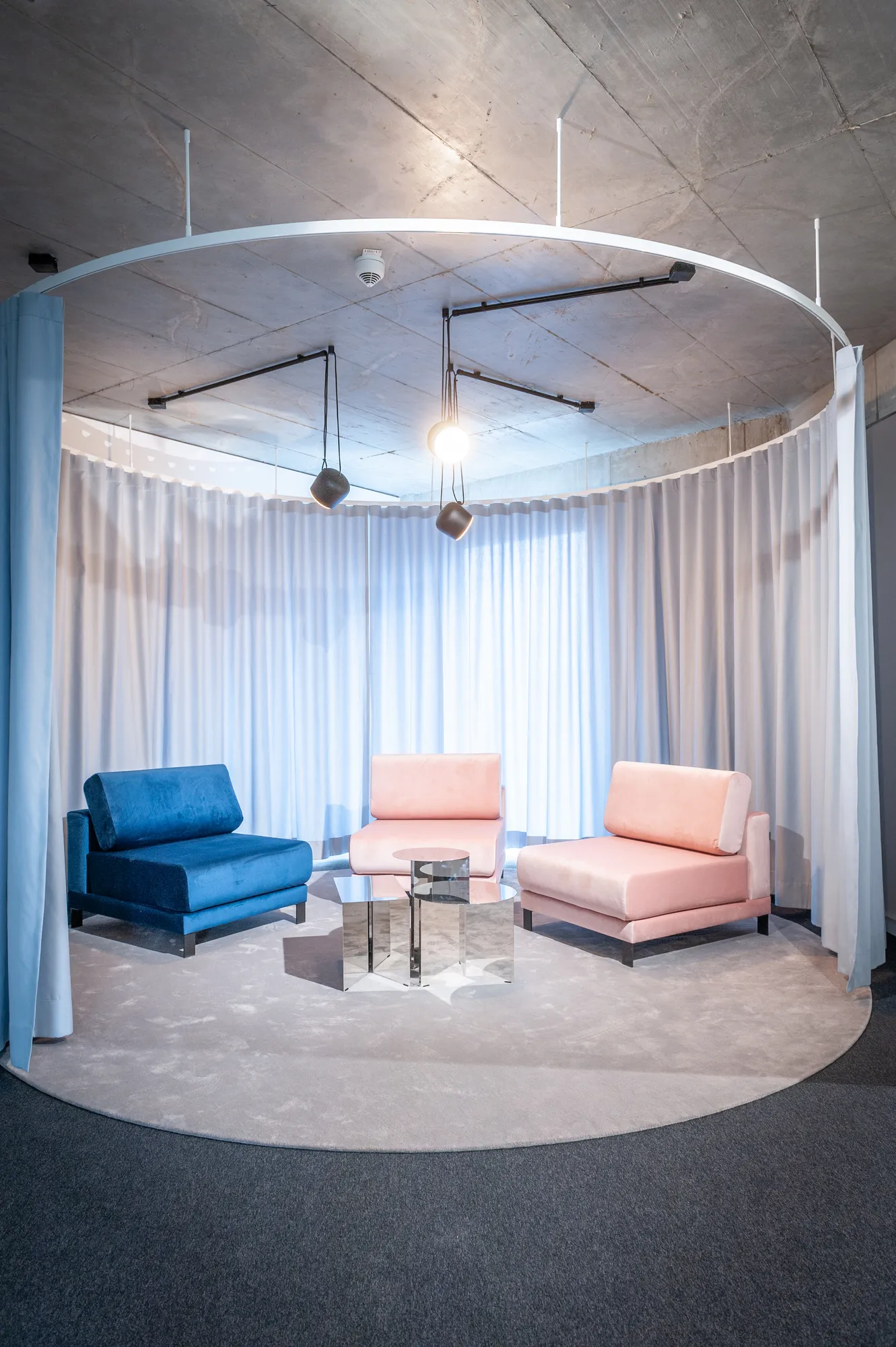 Circular curtained lounge with blue and pink armchairs and a glass side table.