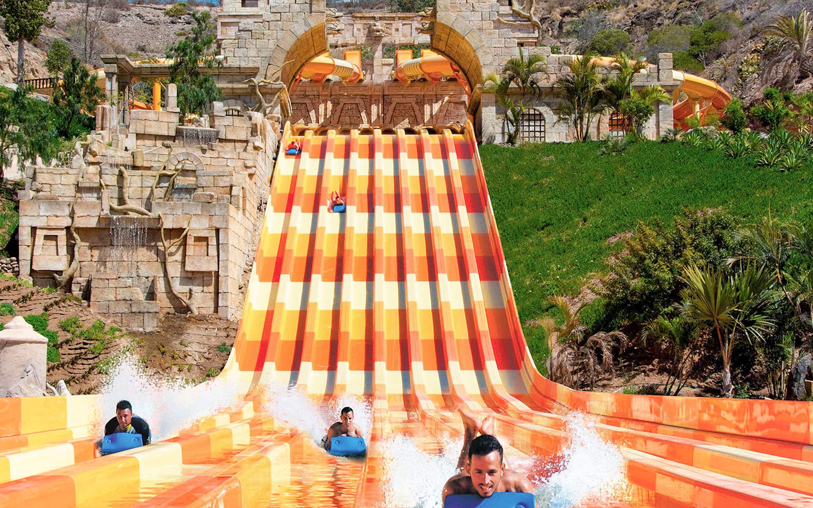 Wasserrutsche im Aqualand Maspalomas, auf der Menschen auf Matten hinunterrasen.