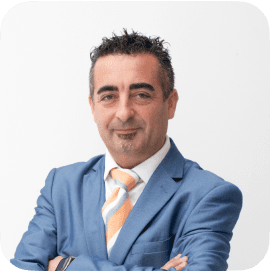 Man in glasses wearing a grey suit and blue tie, looking at the camera with a calm expression.