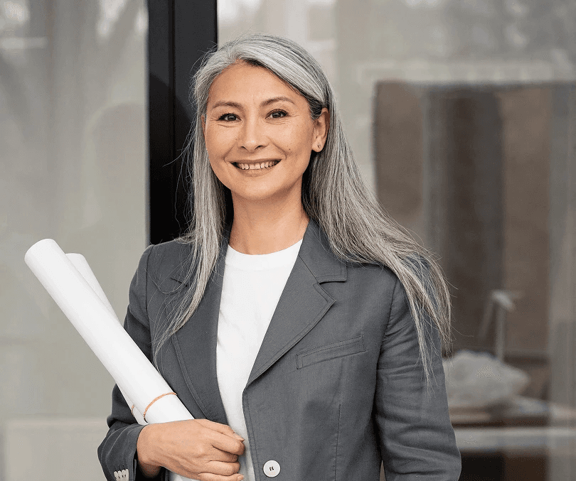 Smiling woman with long gray hair holds rolled blueprints and a solar panel. She's wearing a gray suit, conveying professionalism and eco-focus.
