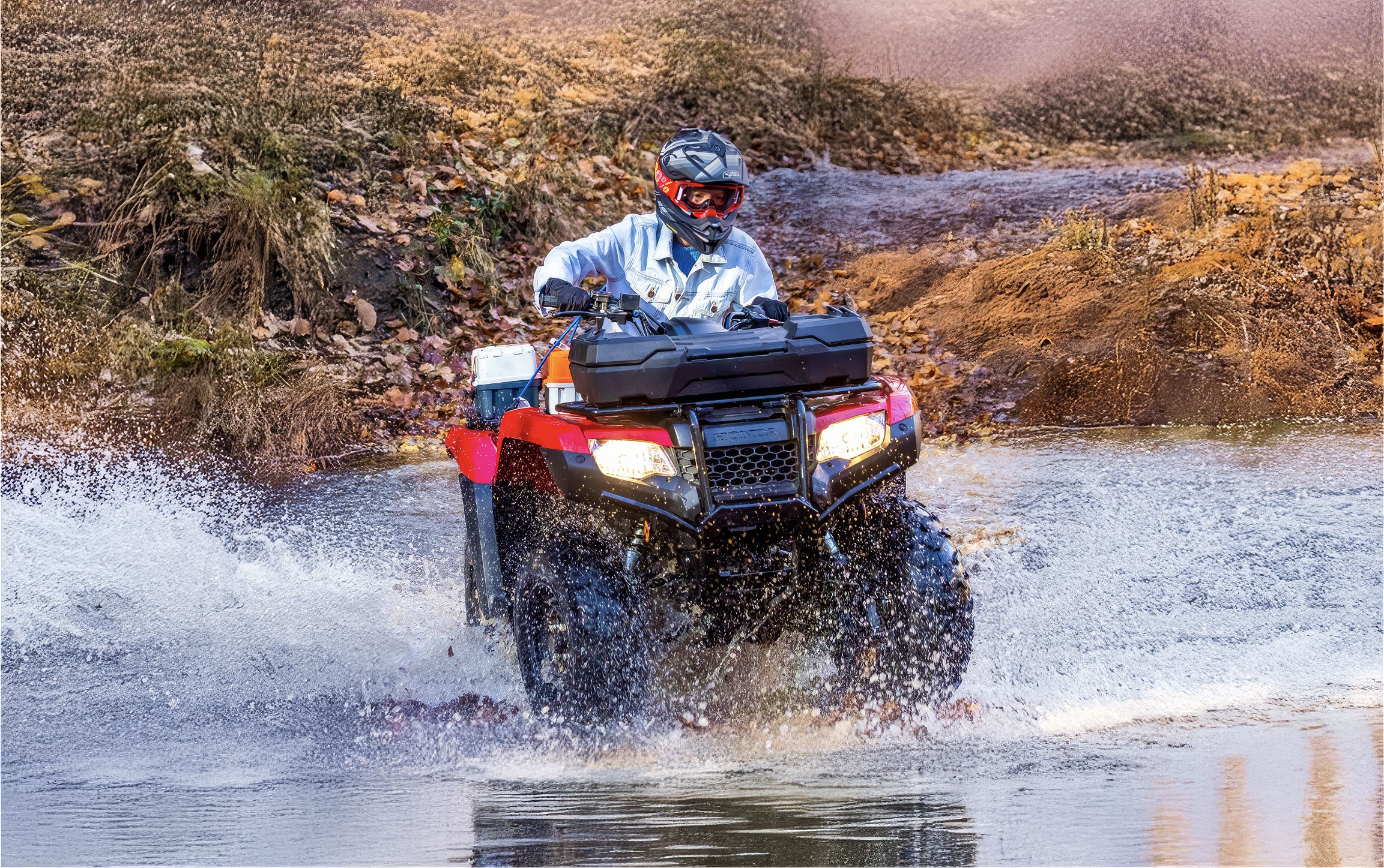 Person riding a red Honda ATV through a shallow stream, water splashing around.