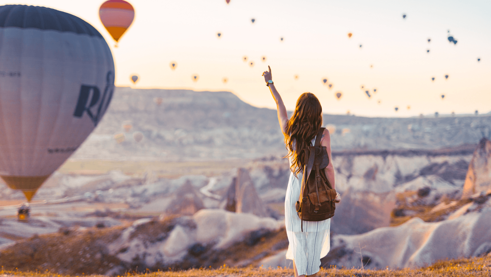 Hot air balloons over Cappadocia, Türkiye at sunrise with a traveler enjoying the view