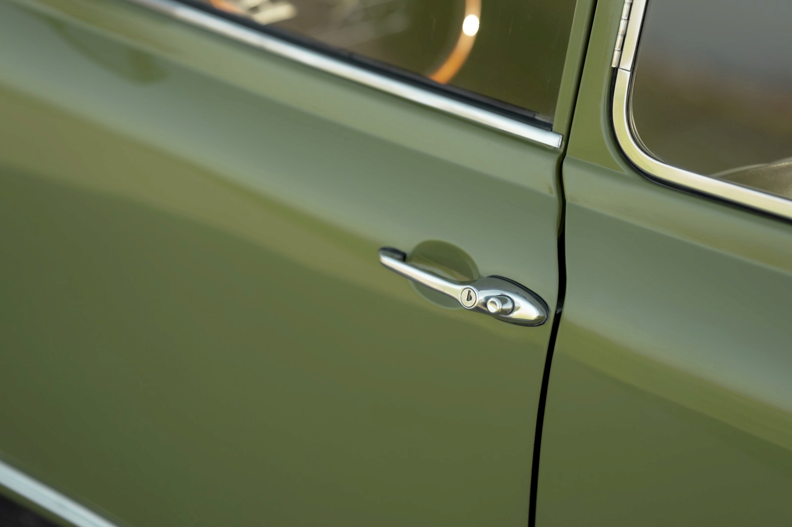 Close-up of a vintage car door, showcasing its green paint and chrome handle. Natural light highlights the finish.
