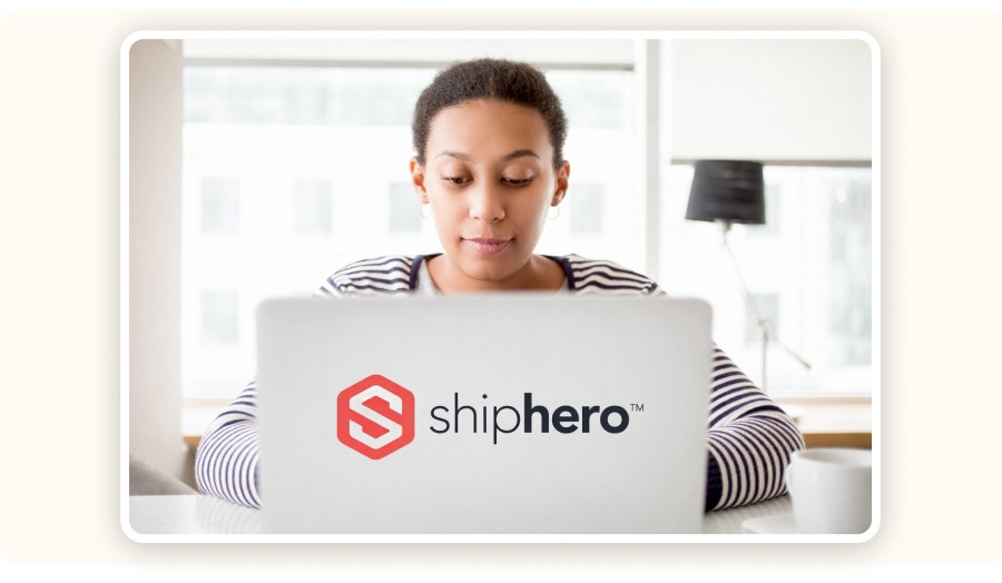 Woman using laptop with ShipHero logo displayed on screen in bright workspace