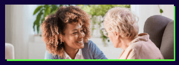 Care worker talking and smiling with an elderly woman indoors.