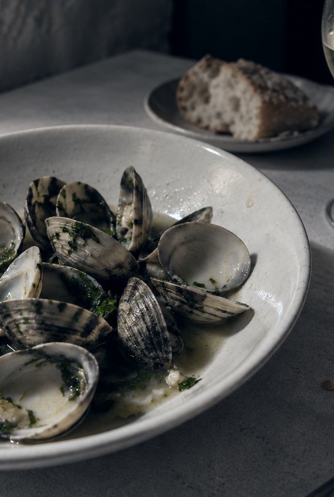 A bowl of lagoon clams with garlic and coriander on a white cloth