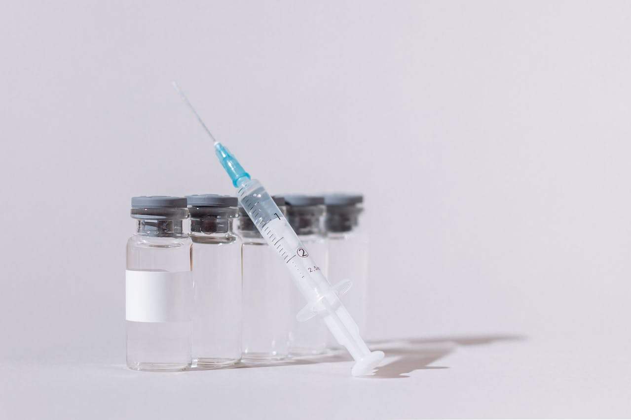 A syringe is leaning on glass vials placed against a gray background.