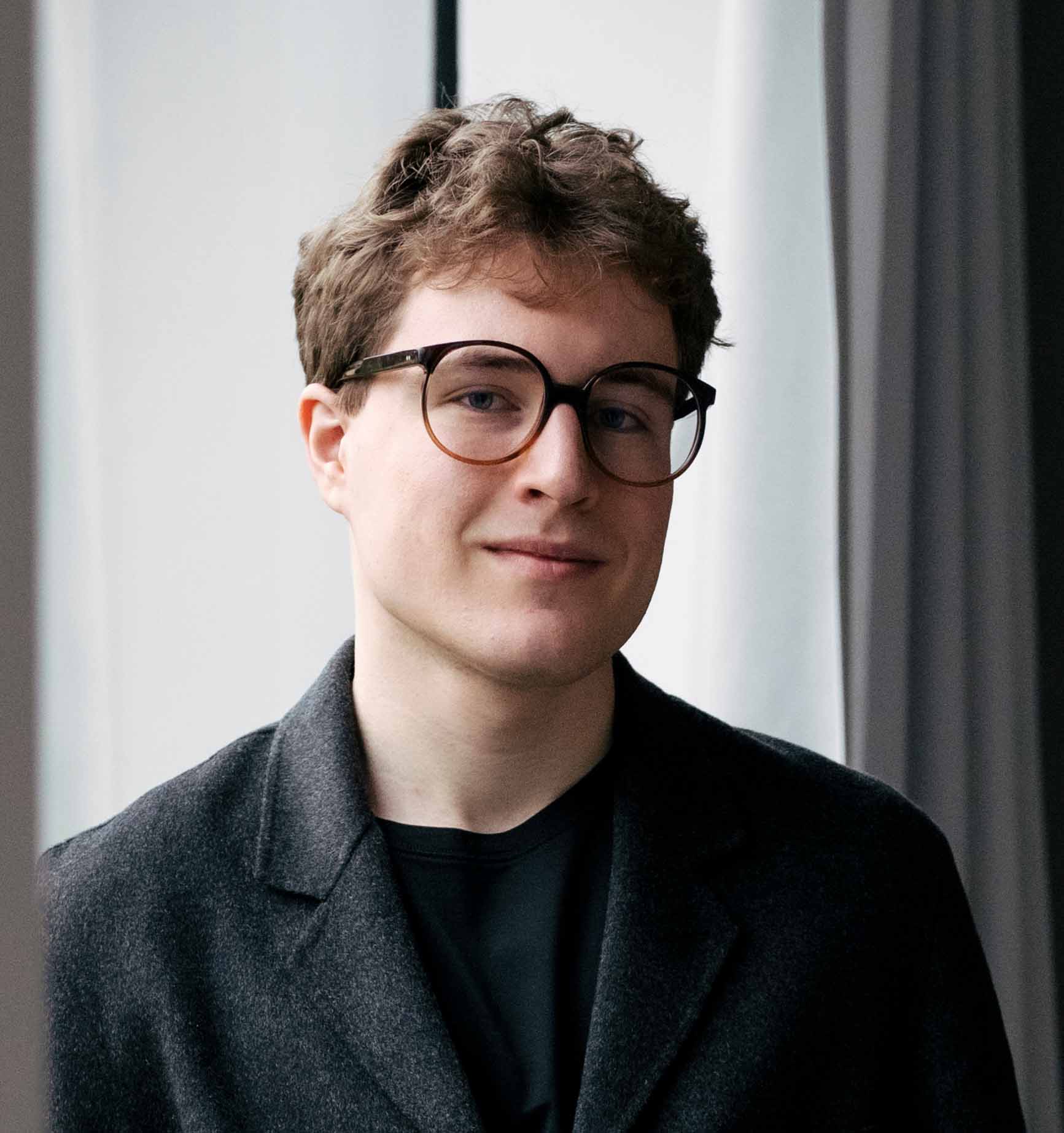 Elke Stoll-Weber mit kurzen dunklen Haaren und schwarzem Hemd lehnt entspannt an einem Holztisch in einem hellen Raum