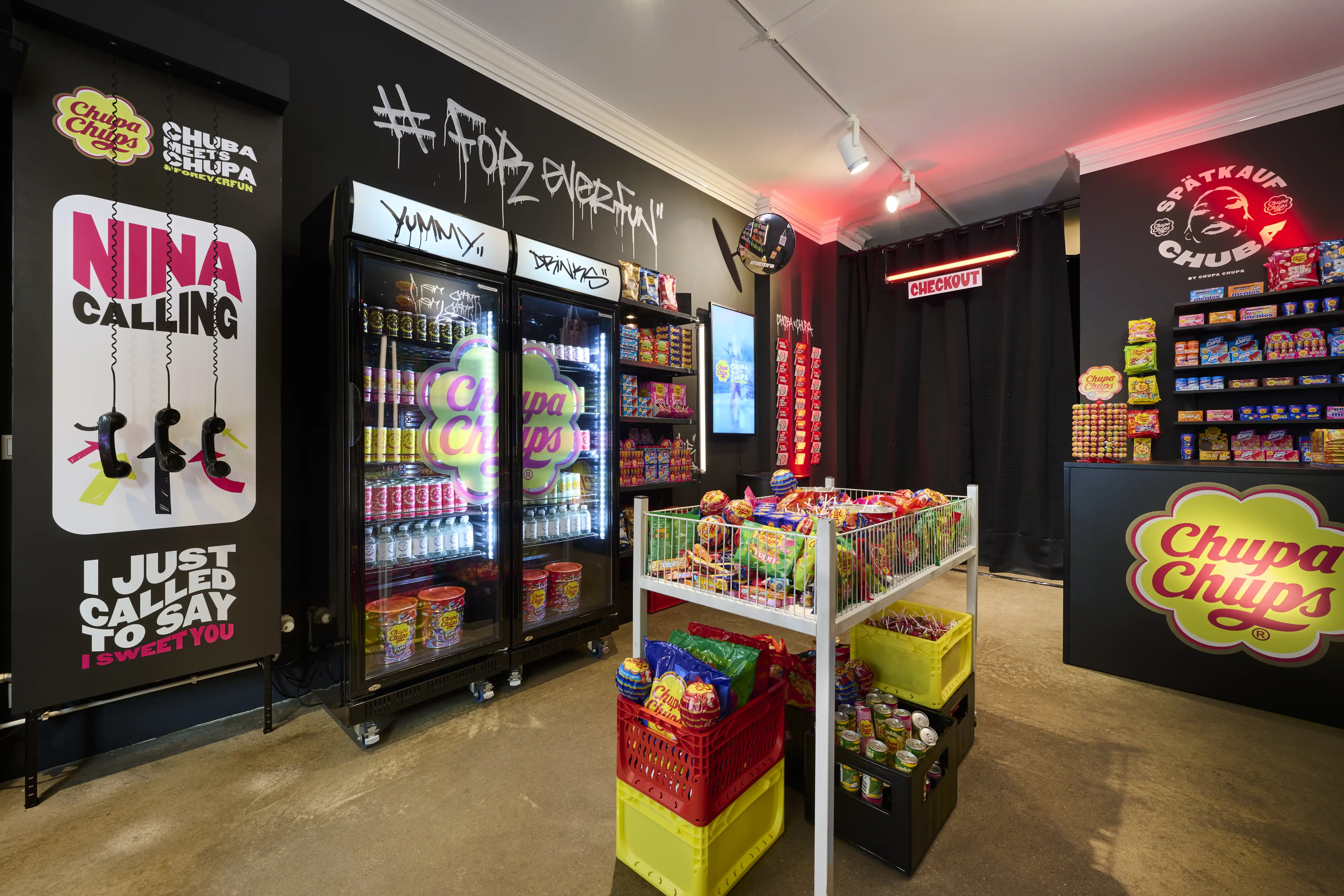 Chupa Chups pop-up kiosk with Nina Calling poster, fridges, candy cart and yellow logo counter under graffiti lettering.