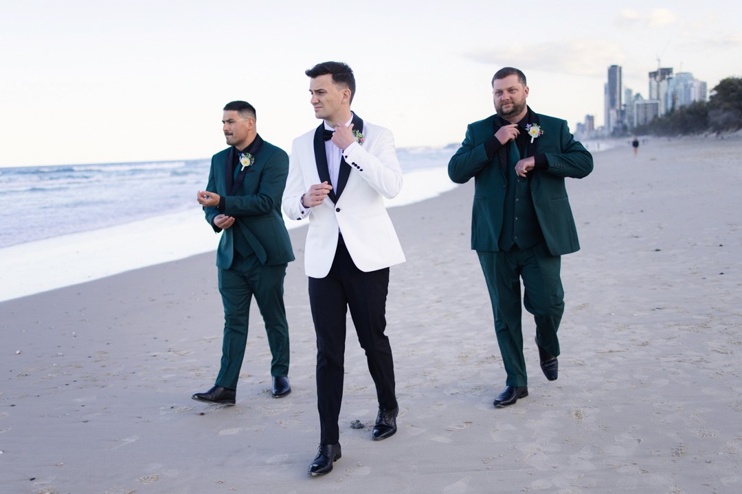 Groom and two groomsmen walking down the beach