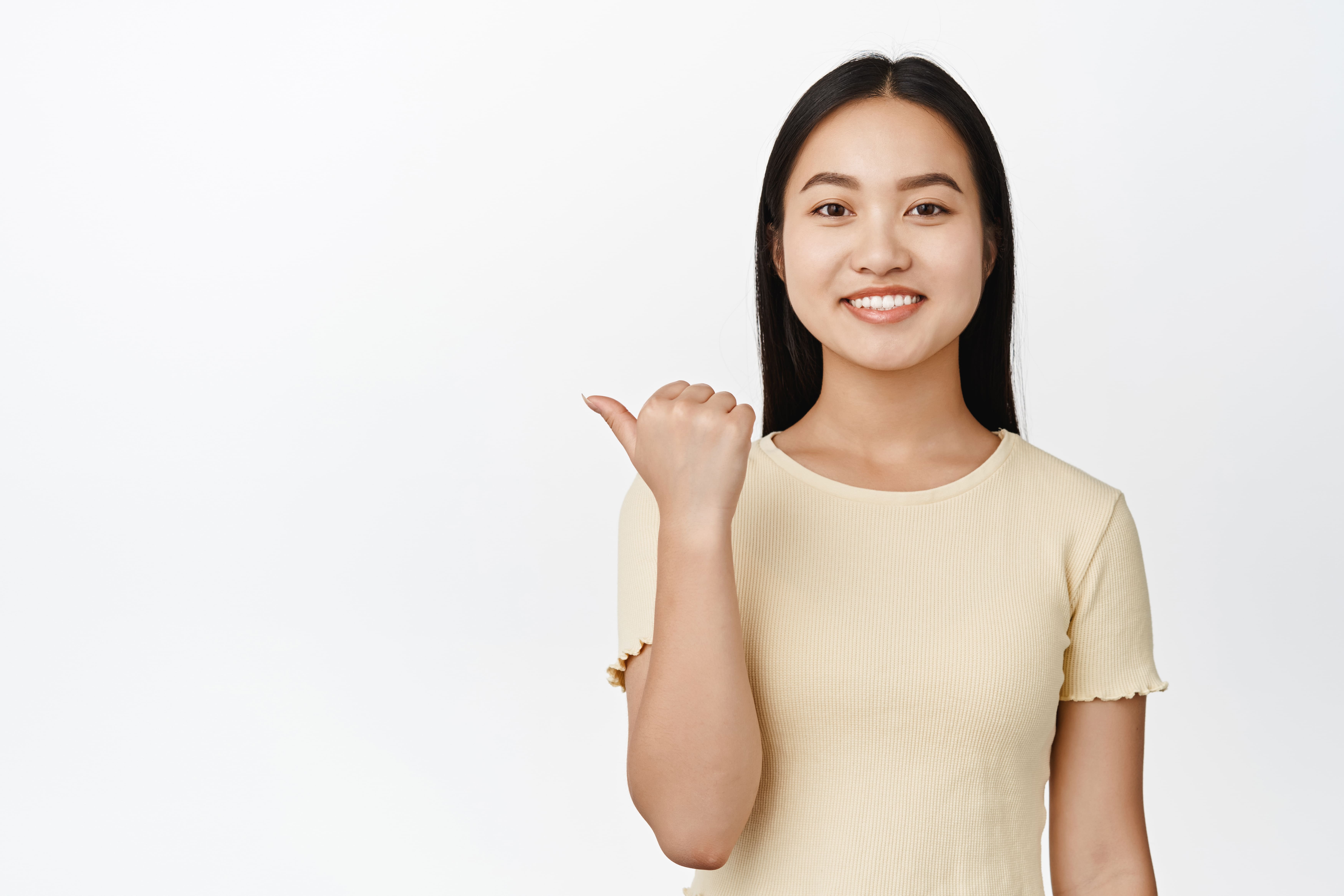 A smiling young woman with long hair, wearing a light-colored shirt and pointing to the left