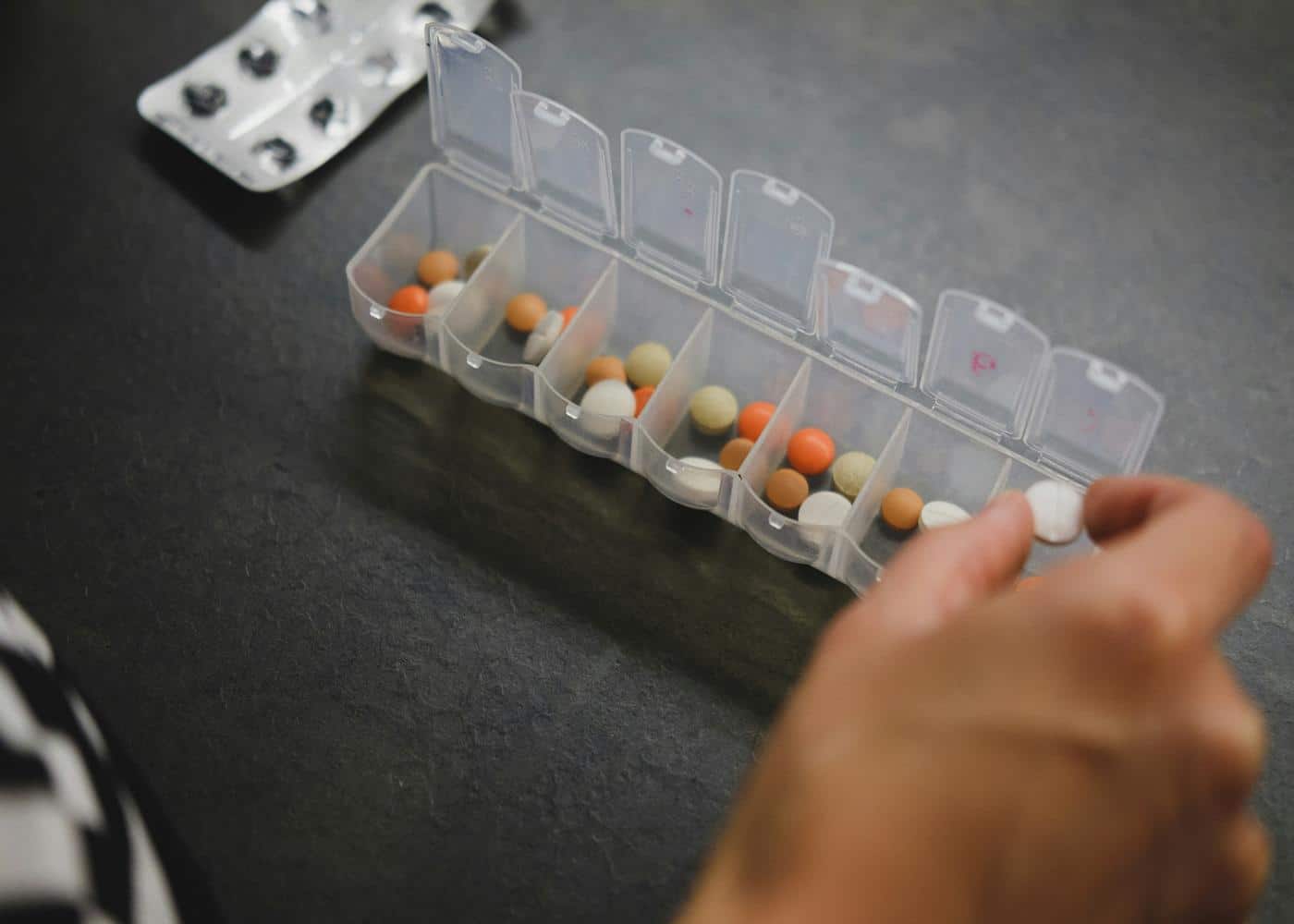 Someone's hand placing sleep supplements into a daily pill case