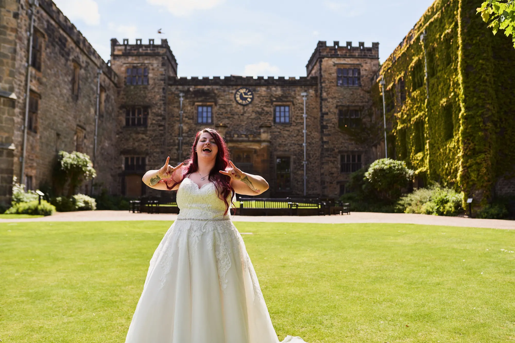 Bride throwing her arms wide with joy on the lawn in front of Towneley Hall’s battlements in Burnley