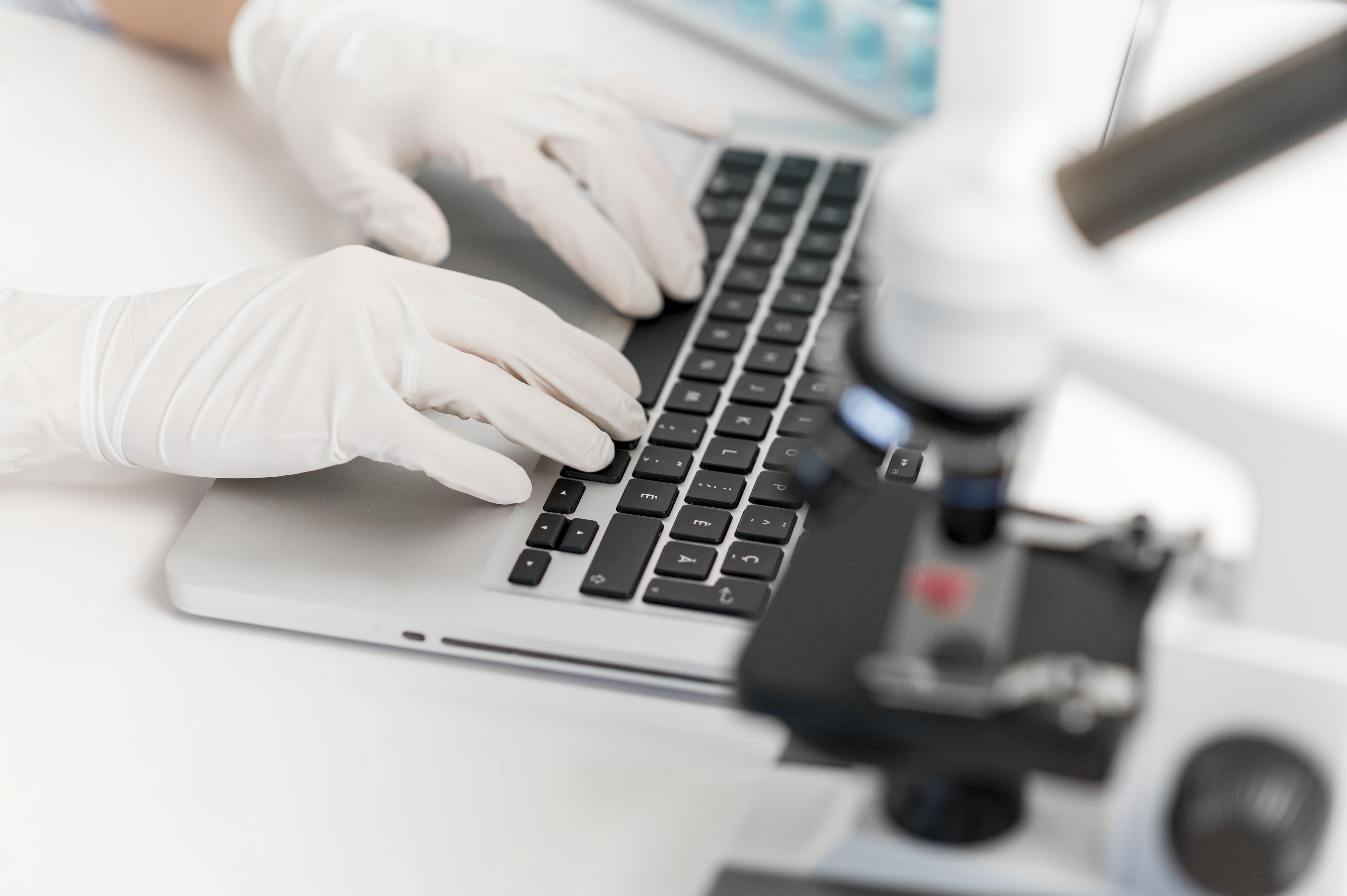 A scientist in white gloves using a laptop, working on solutions for biopharmaceutical manufacturing automation.