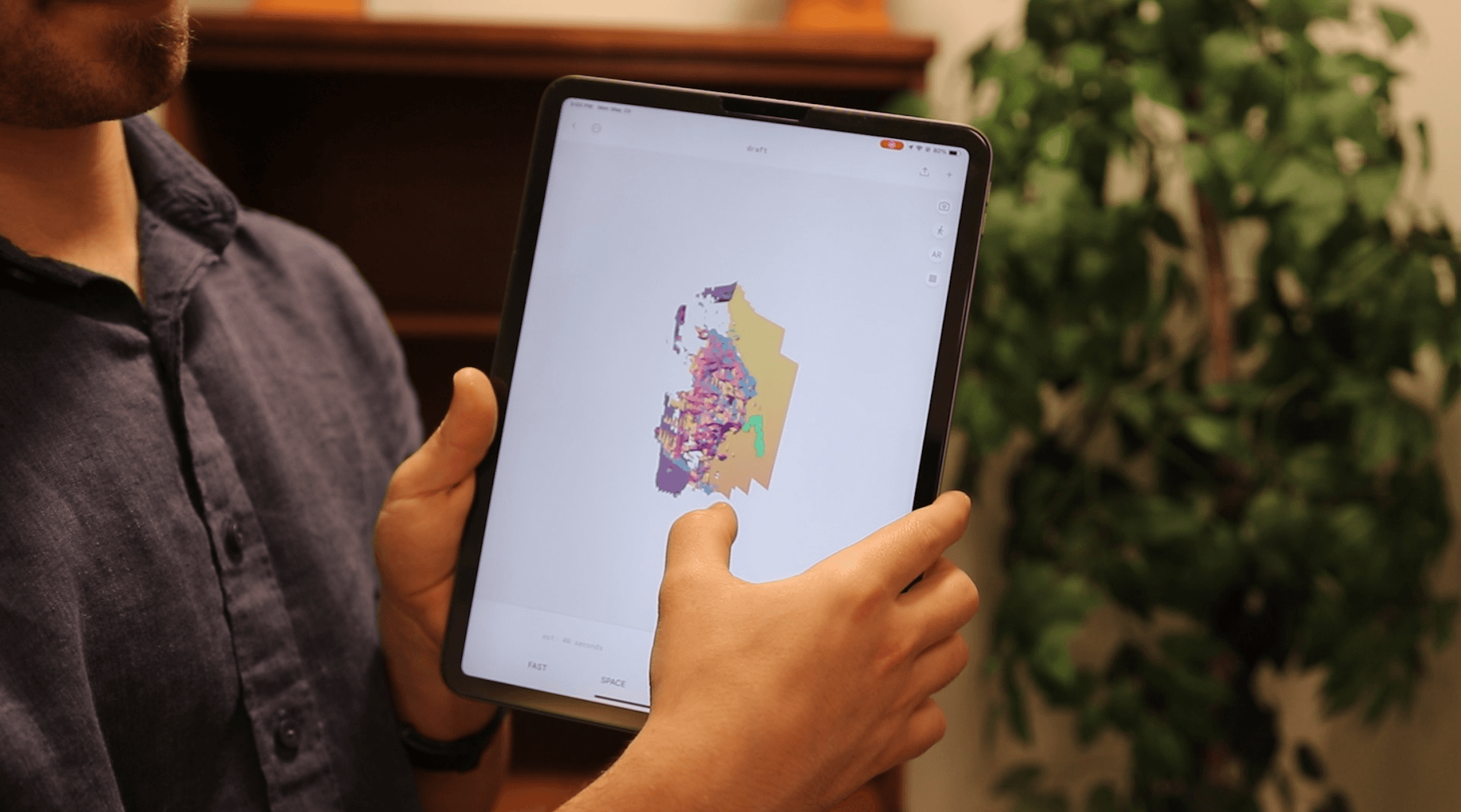 Person holding a tablet displaying a colorful geographic map or data visualization—representing geospatial analysis or interactive data tools.