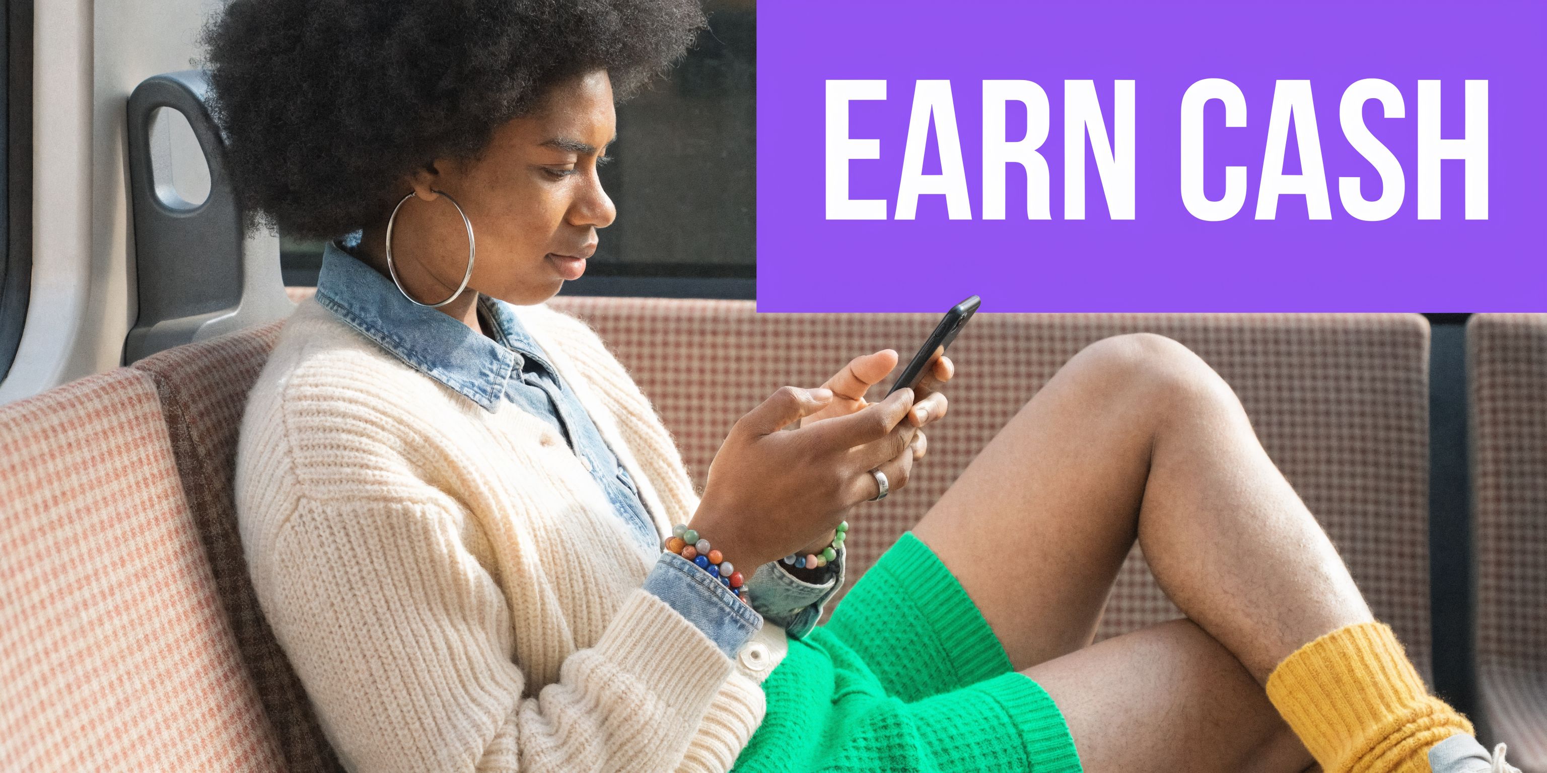 A young woman with curly hair sitting on a train while using her smartphone to earn money.