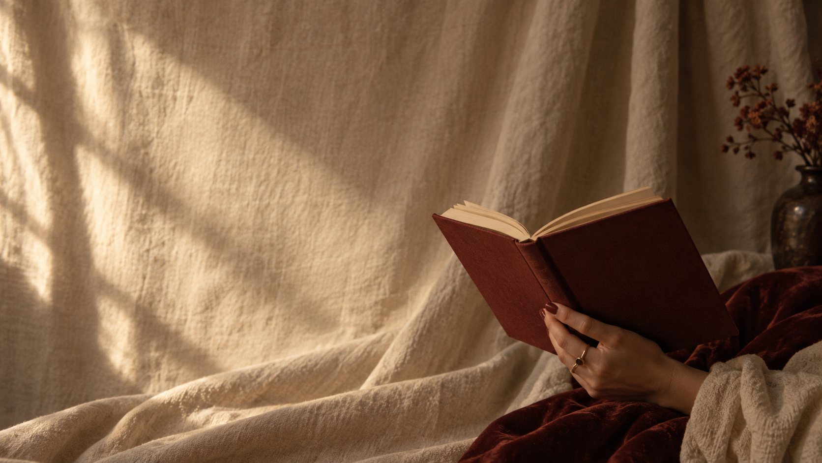 A hand holding an open red book against soft linen