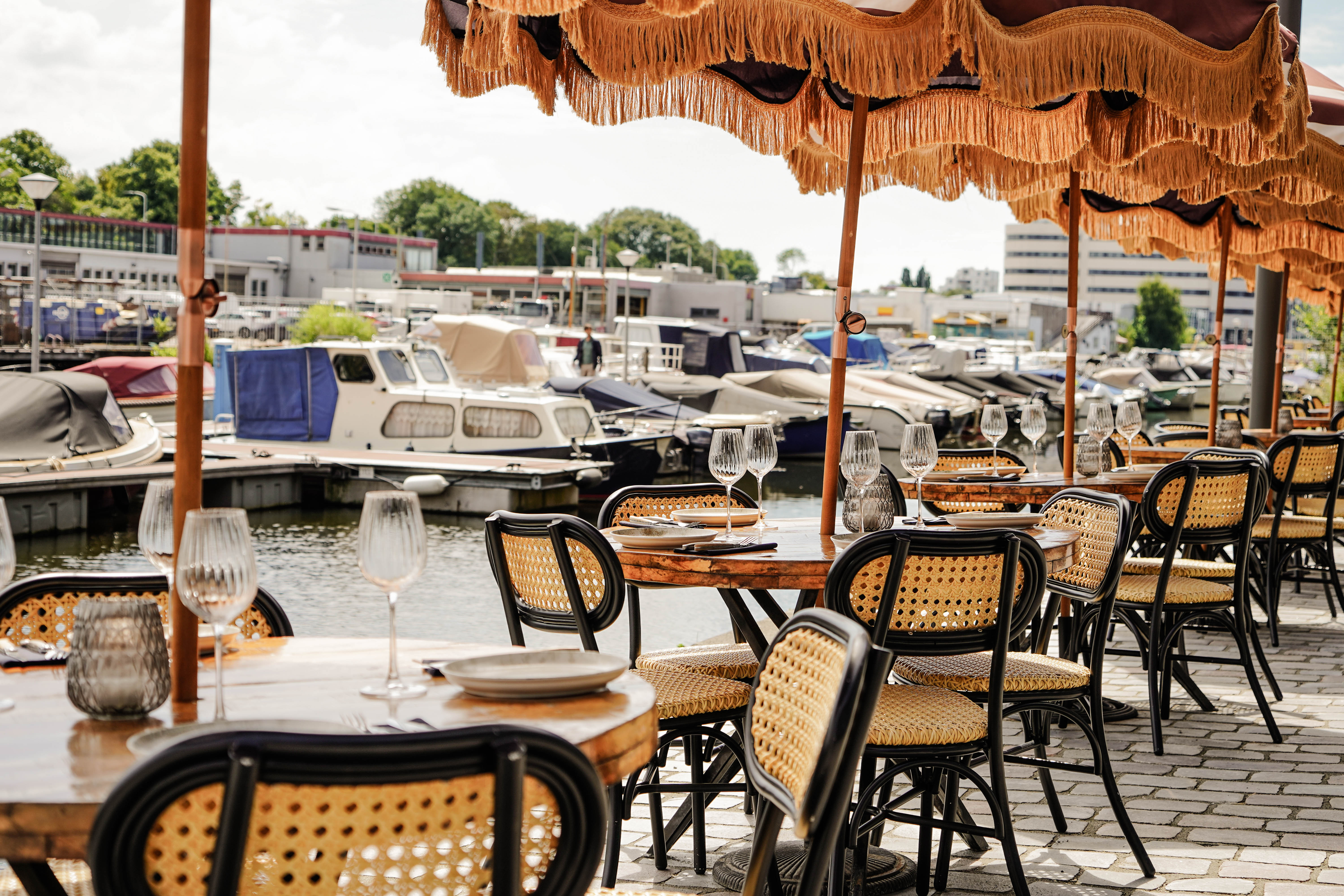 terrace in a small harbour with umbrellas, boats and tables