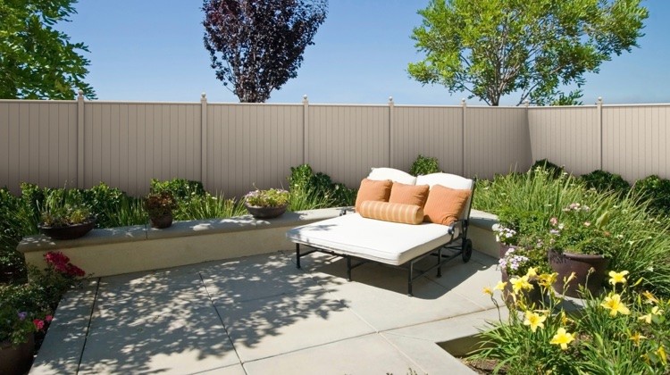 A beautifully landscaped backyard patio featuring a modern outdoor lounge area, enclosed by a tall, solid aluminum privacy fence.