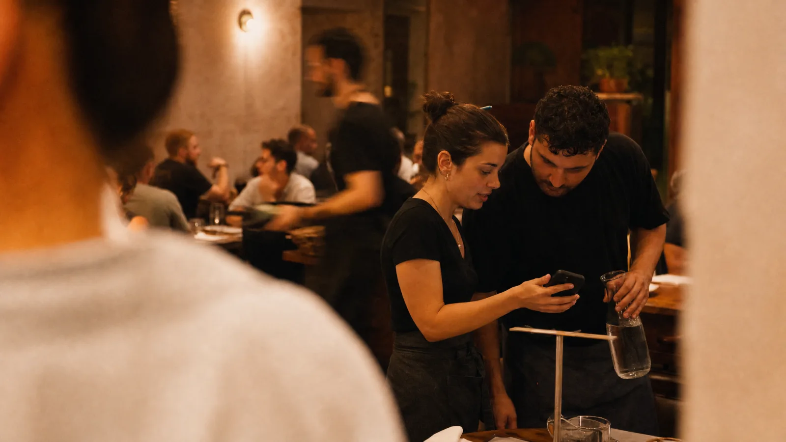 Responsabile di pizzeria mostra a un cameriere come inquadrare col telefono il QR sul tavolo