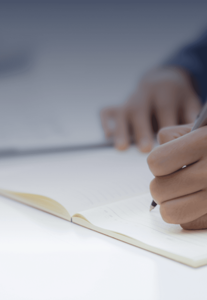A close-up of a person's hand writing on a piece of paper with a pen, on a light surface.