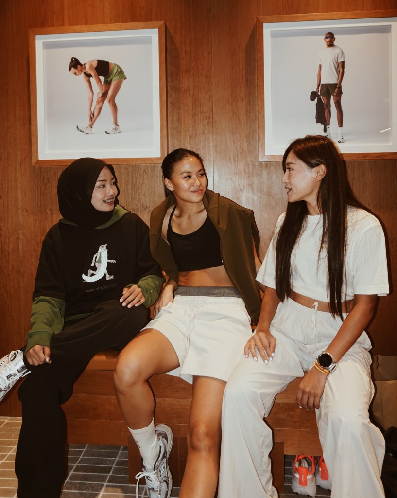 Three women sitting together in a casual setting, smiling and engaging in conversation, with running and athletic-themed artwork displayed in the background.