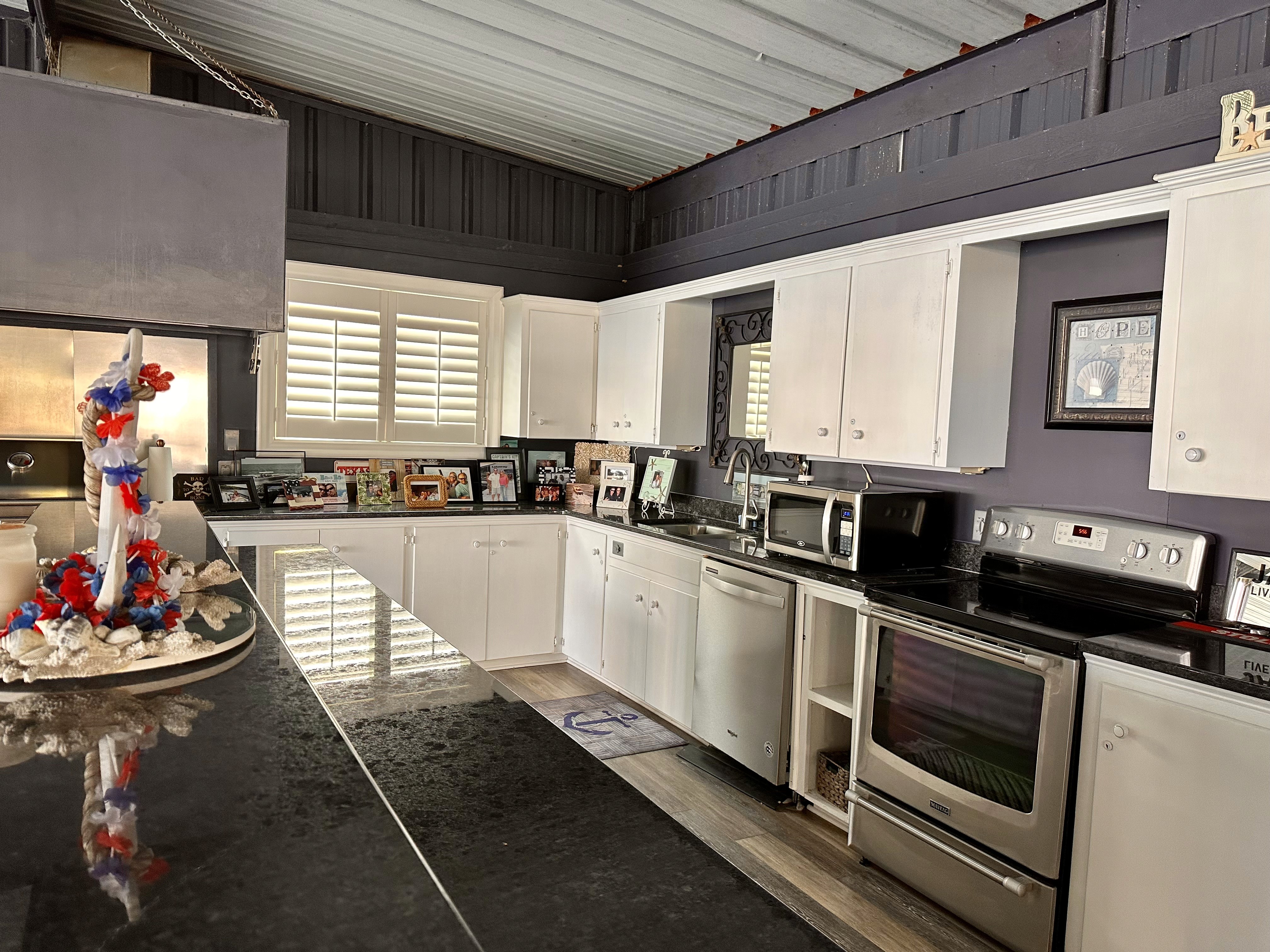 The image shows a modern kitchen with black granite countertops, white cabinets, and stainless steel appliances, adorned with various decorative items and picture frames, creating a cozy and personalized space.
