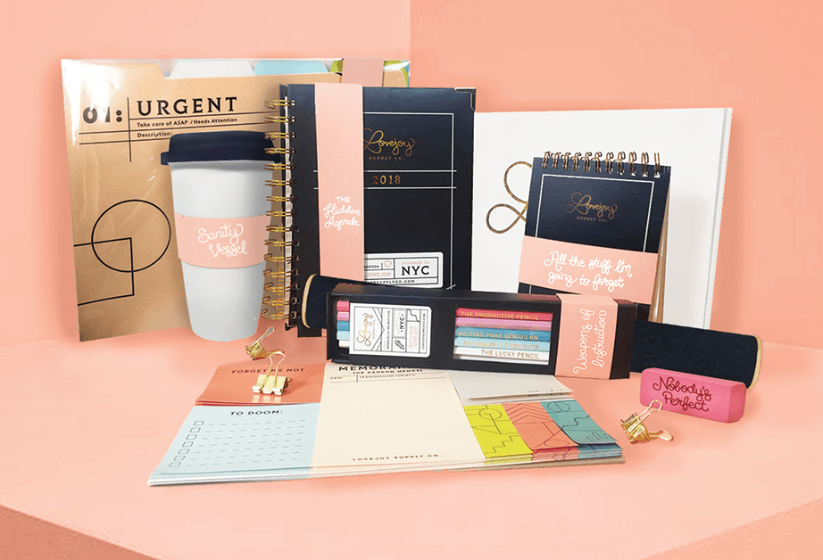 A collection of stationery and planners from Lovejoy Supply Co., featuring a dark navy spiral-bound planner labeled "THE HIDDEN AGENDA," a daily planner with matching branding, and a white envelope with the company logo, all set against a light beige background.