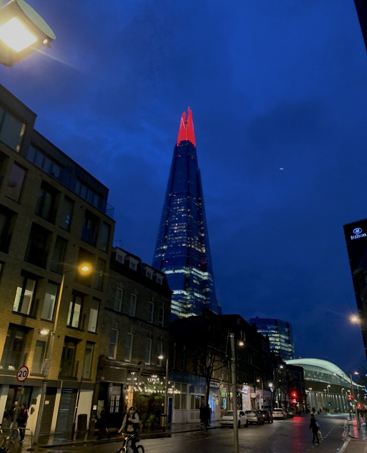 A smiling young man with crossed arms, wearing a plaid shirt and white t-shirt, poses against a dark background.