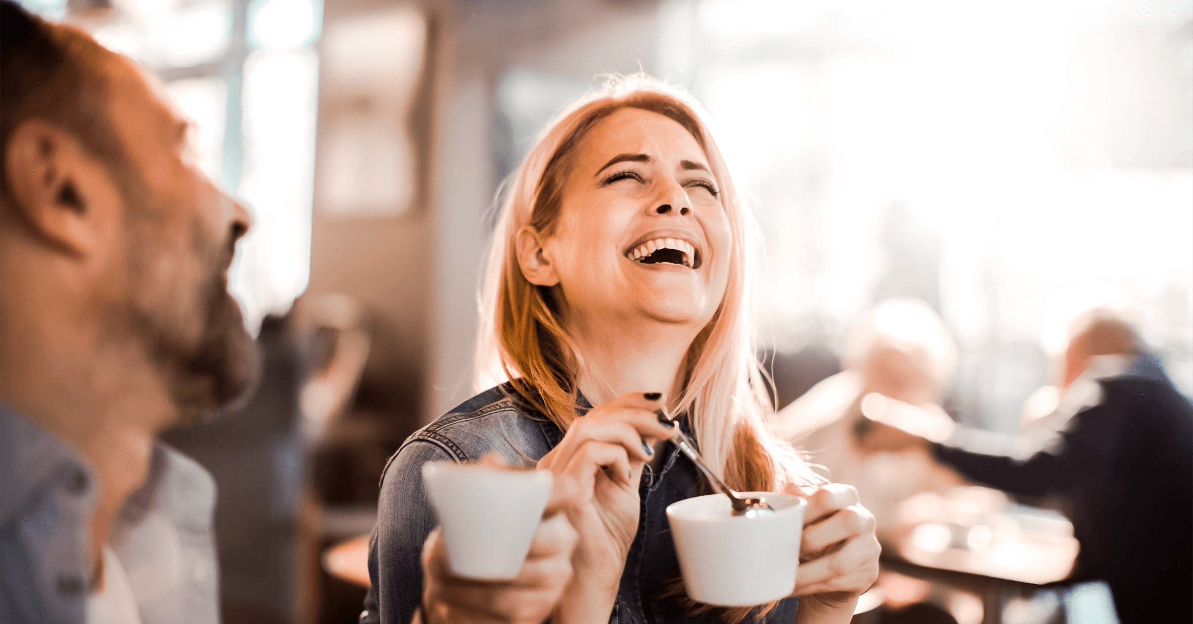 En kvinne er på date med en mann på en kafé. Fokuset er på kvinnen, som ler og smiler.