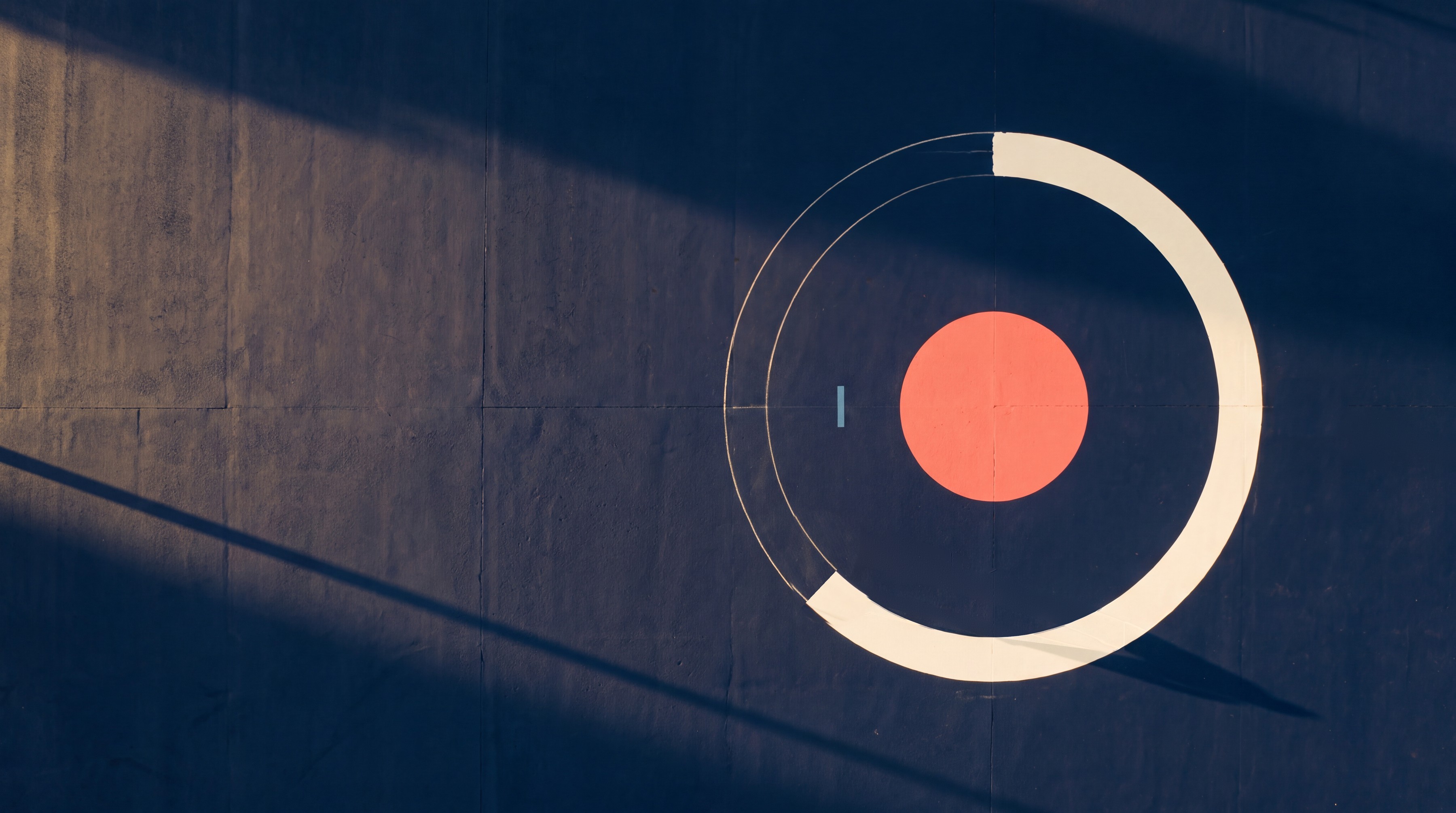 A coral disc inside a cream ring painted three quarters of the way round, on a midnight rooftop seen from directly above, with small groups of people walking.