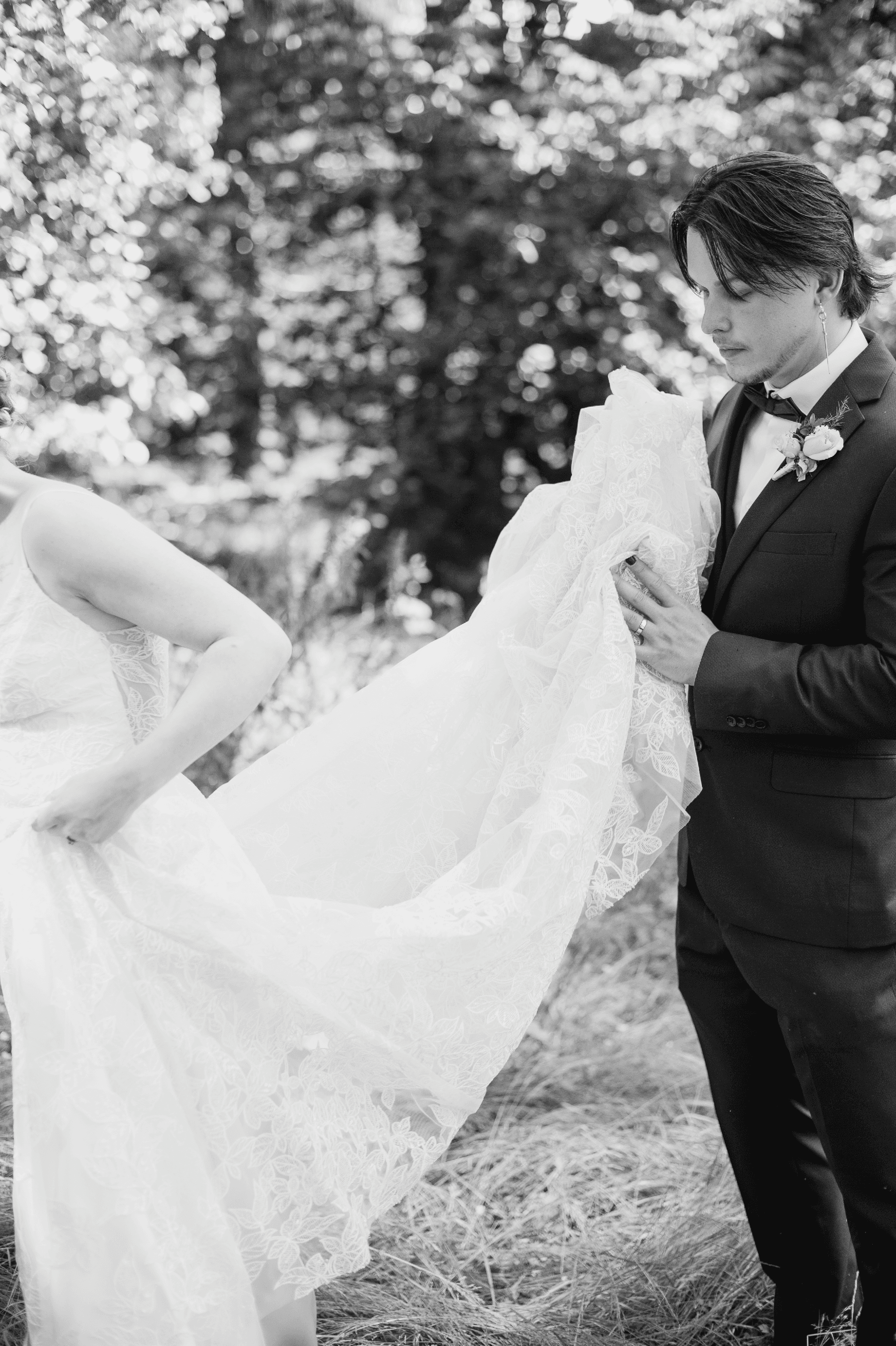 Black and white photo of a wedding couple image of the groom holding the brides dress.
