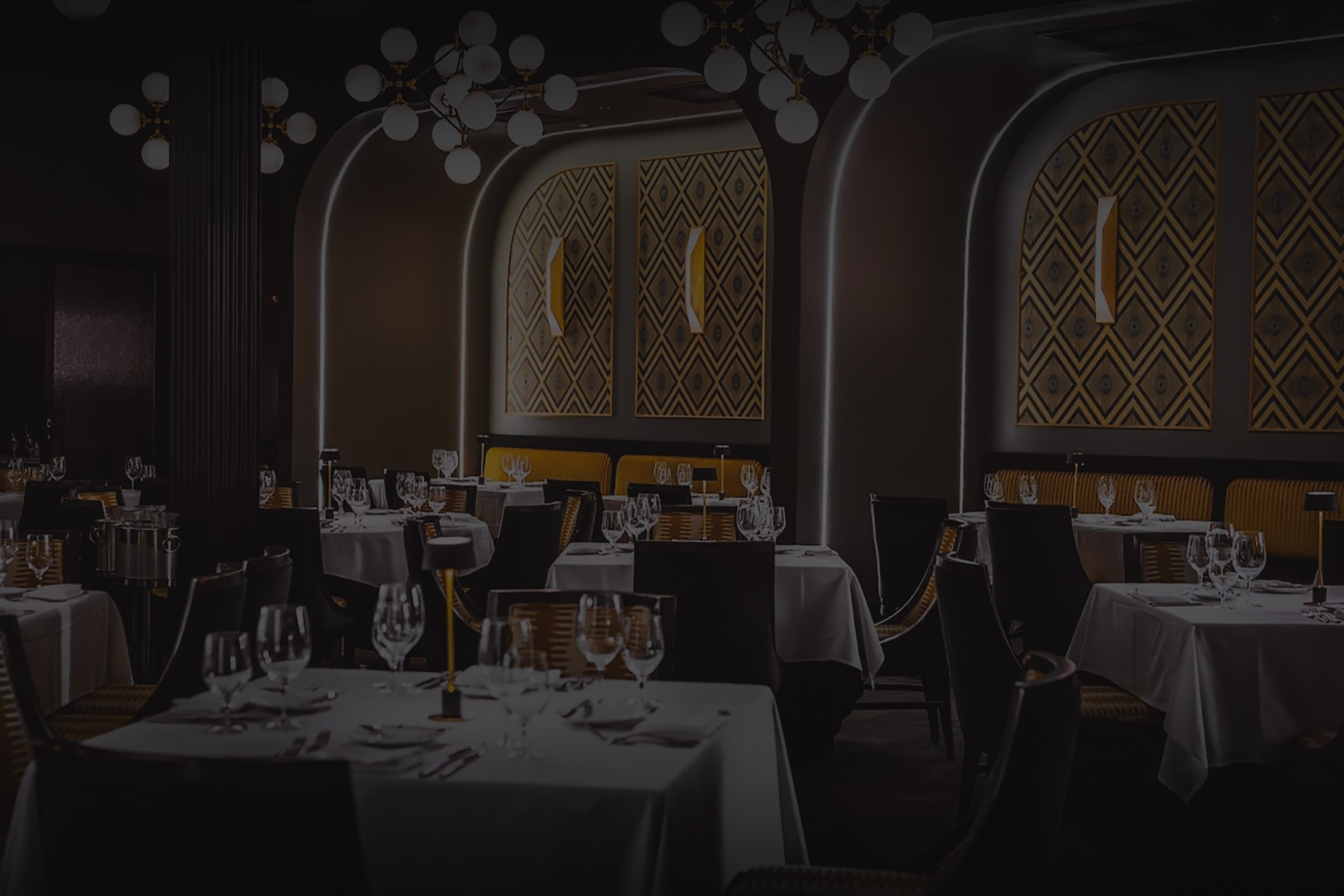 Elegant dining room with white tablecloths, dark chairs, and gold accents. The room has an art deco design.
