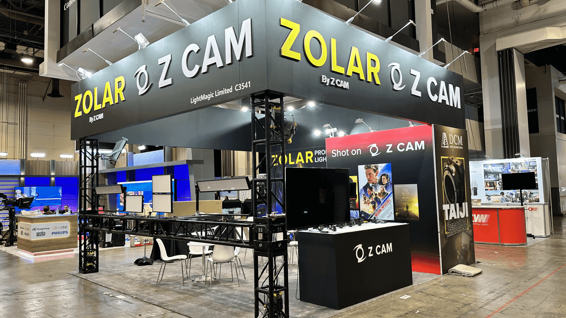 Z CAM and ZOLAR NAB Show 2024 20x20 camera and lighting demo booth with hanging signage, black structural framing, product counters, and aisle-facing display areas