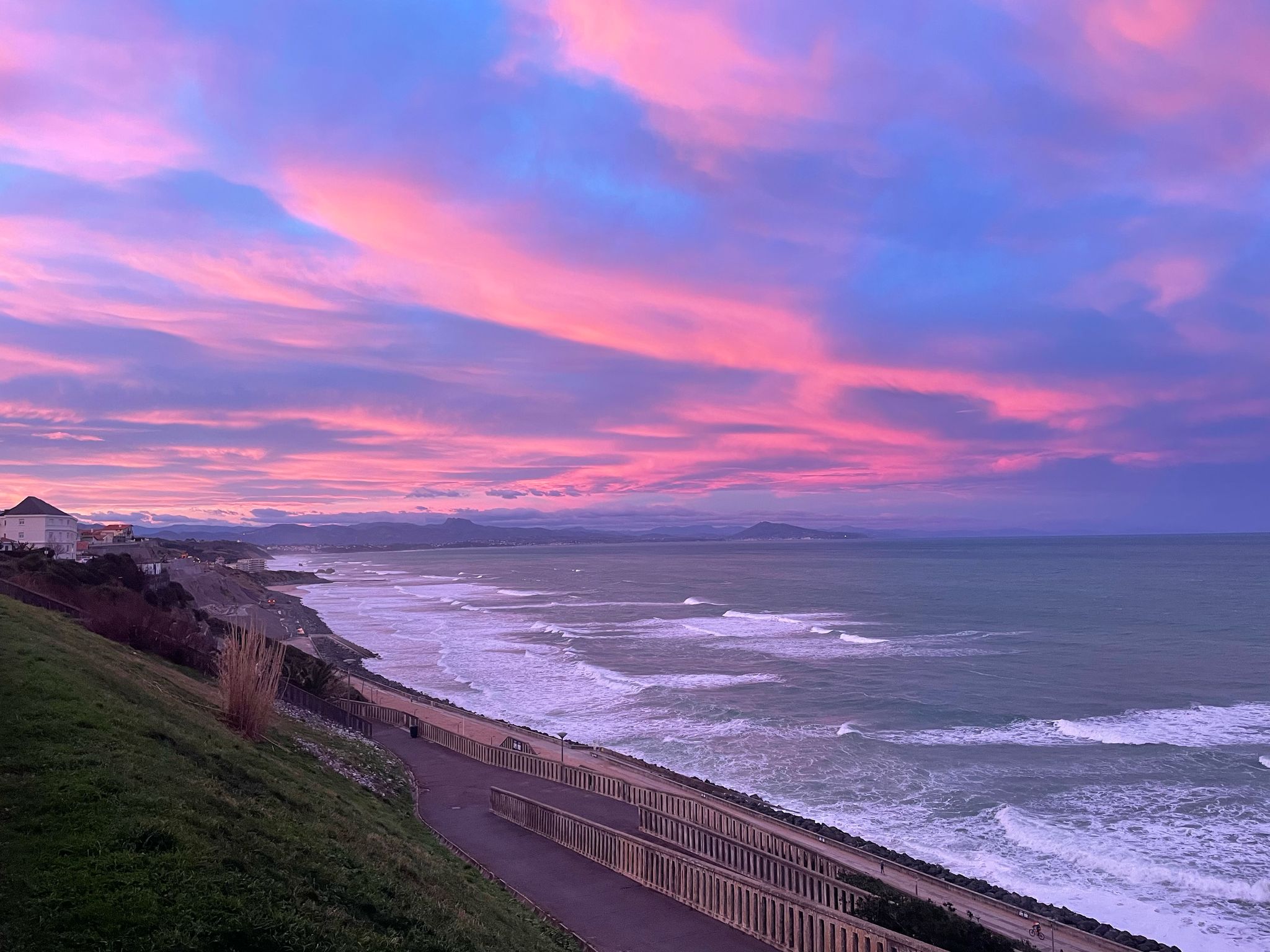 Vibrant pink and purple sunset colors reflected across serene ocean waves and sandy path.