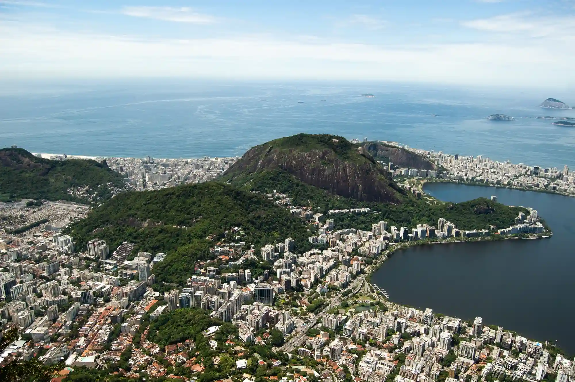 Aerial view of a coastal city nestled around a lagoon and forested mountains, suggesting an exotic travel destination.