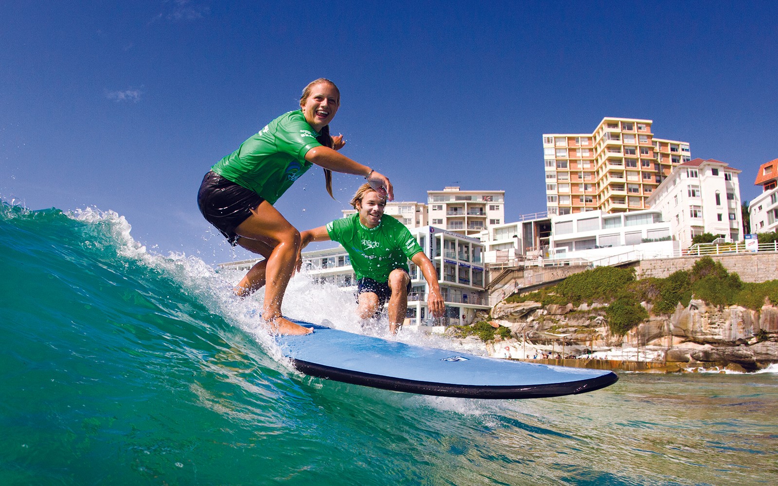 Surfisti che cavalcano un'onda durante una lezione a Bondi Beach, Sydney.