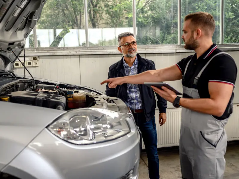 A mechanic talking a customer through a repair under the bonnet