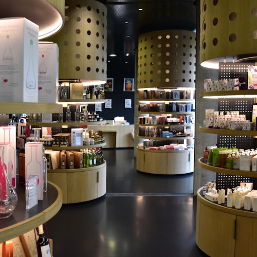 A modern store interior with curved wooden shelves and cylindrical displays, showcasing various bottles, boxes, and products.