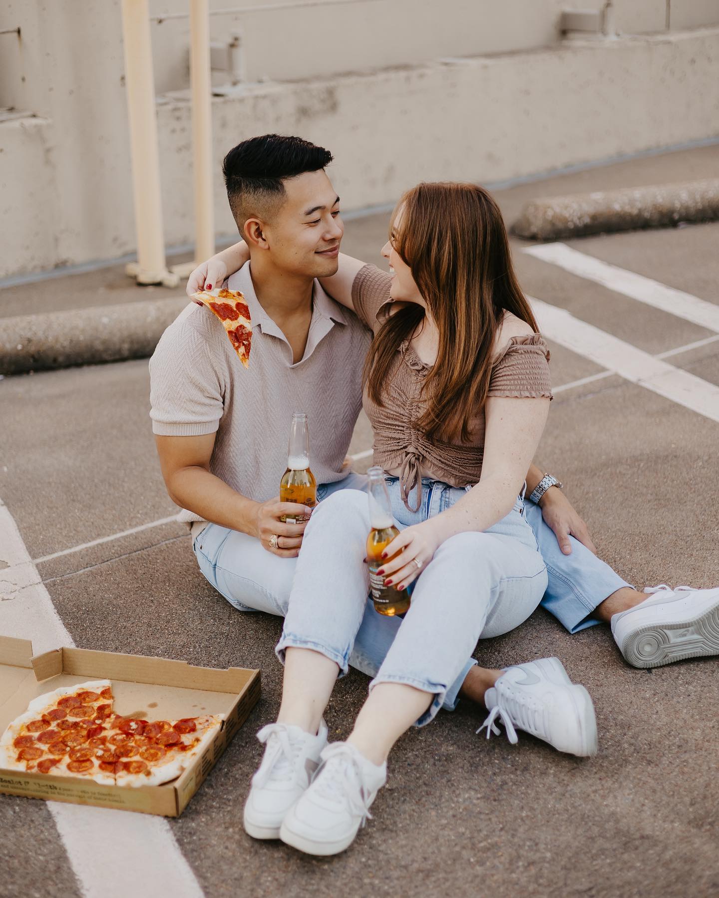 A couple drinking beer and eating pizza in a parking lot