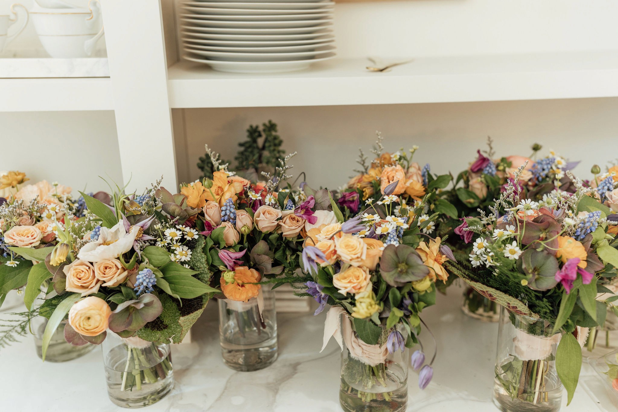 Bridesmaid bouquets of peach roses and delphinium lined up in glass vases.
