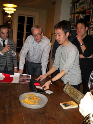 A photo of a couple of people sitting around a table and looking at a person deploying a board game.