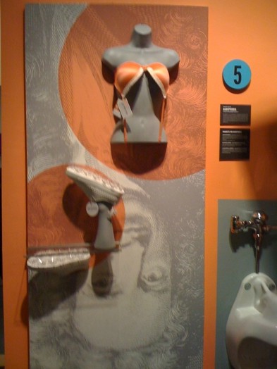 installation view of a mannequin with a bra put upside-down and a fake leg with a shoe on it installed upside down