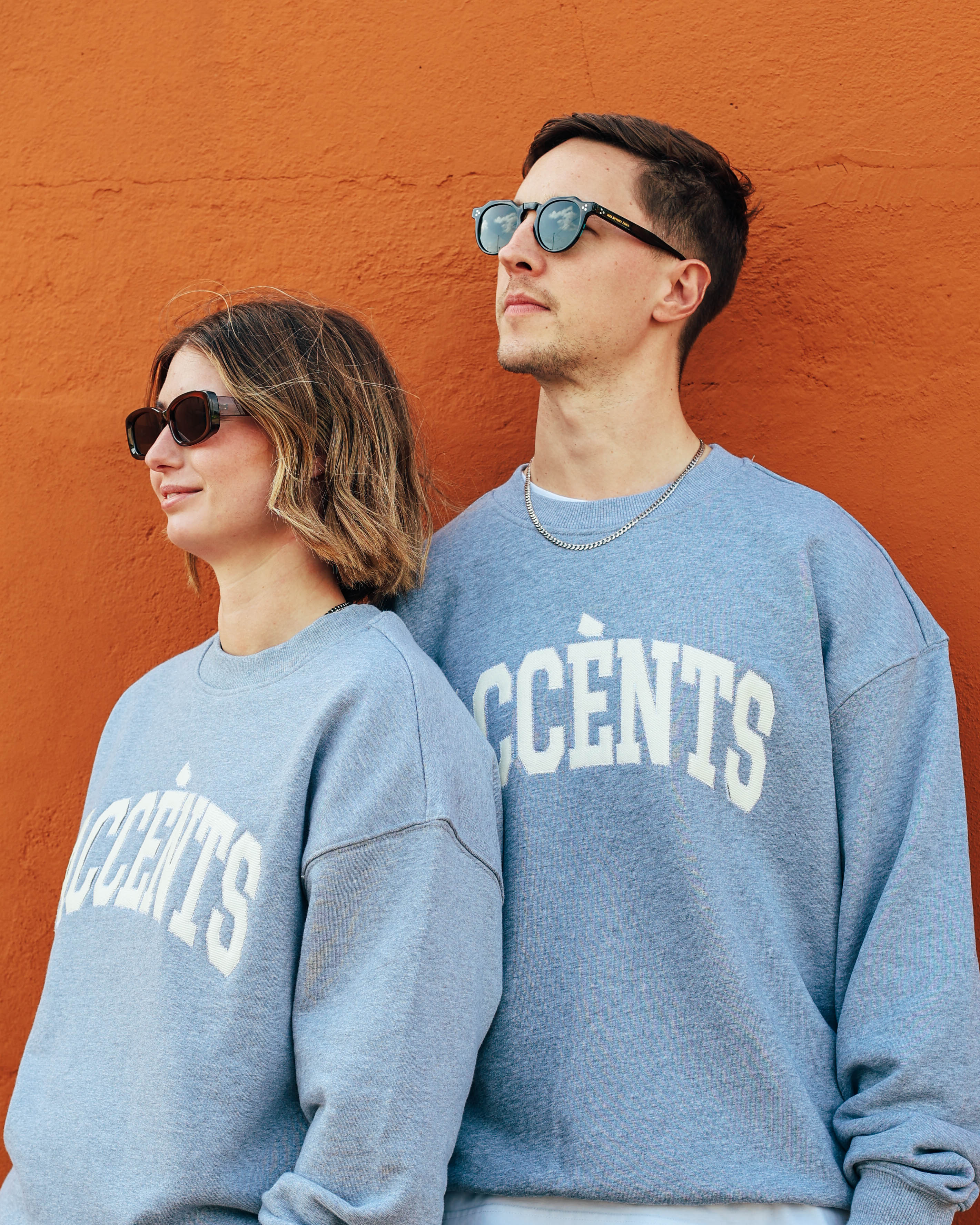 Man and woman in grey sweaters against an orange background